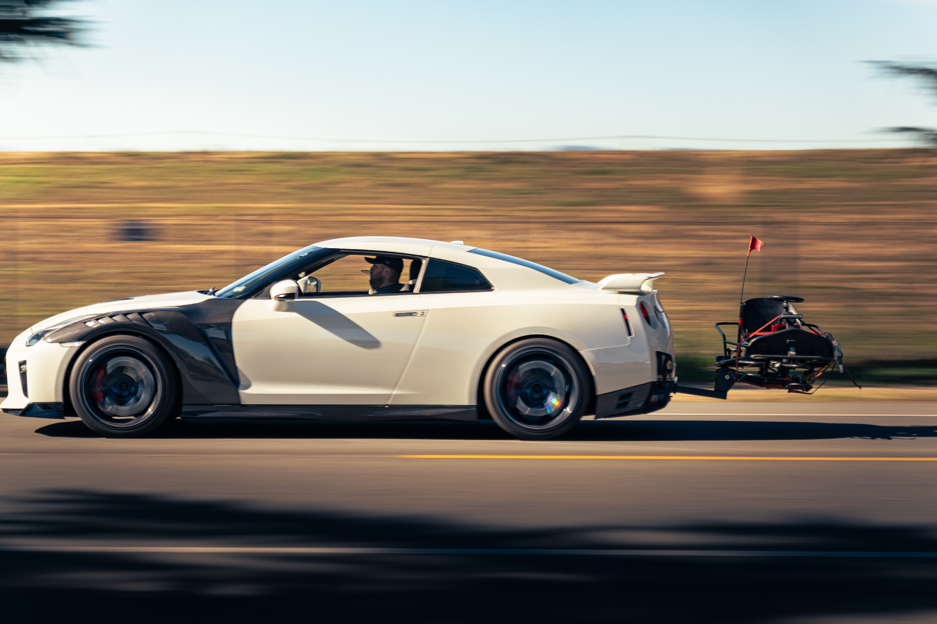 White Nissan GT-R towing a camera rig cruising past the fields