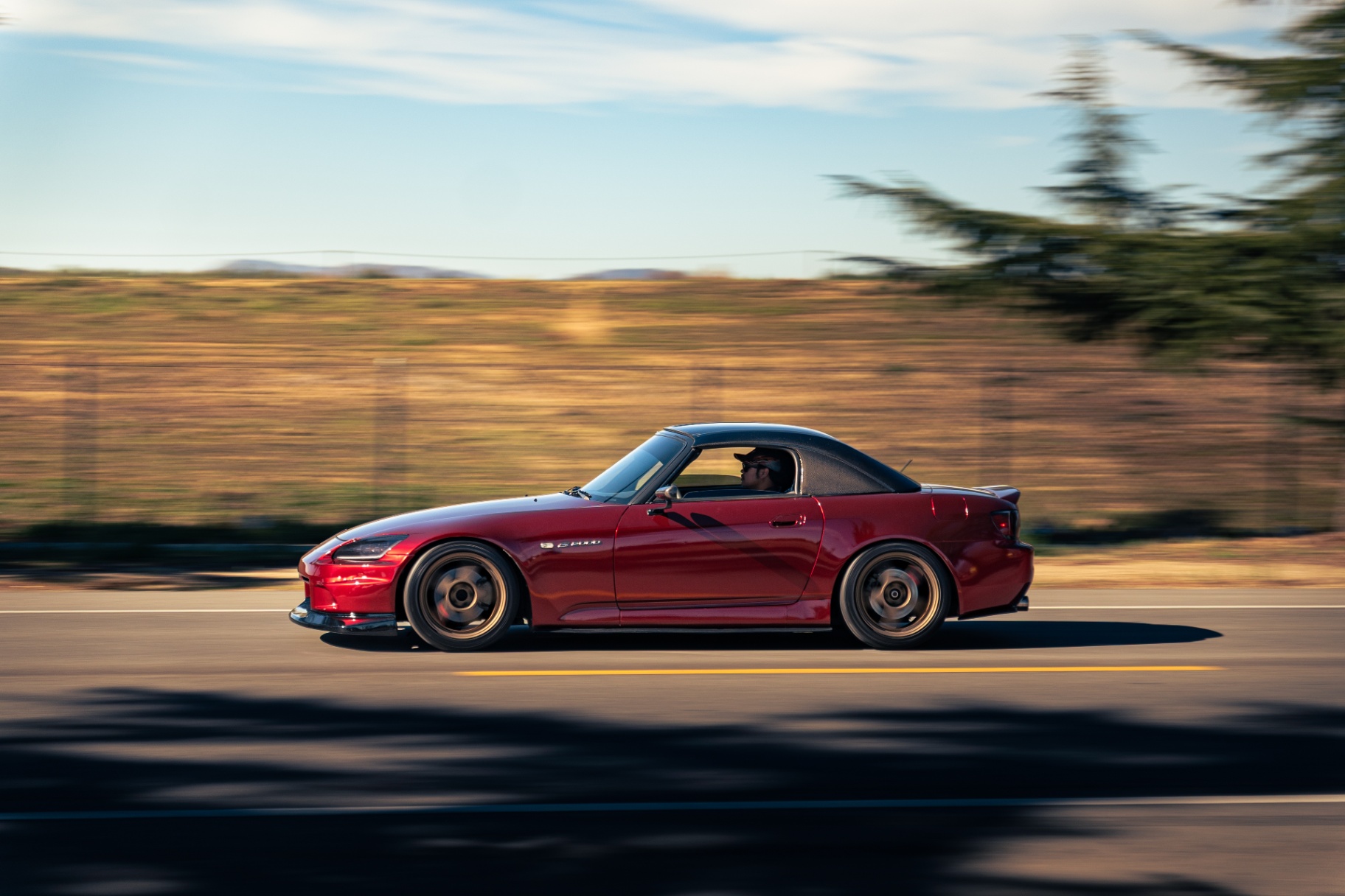 Red Honda S2000 with hardtop panning down the open road
