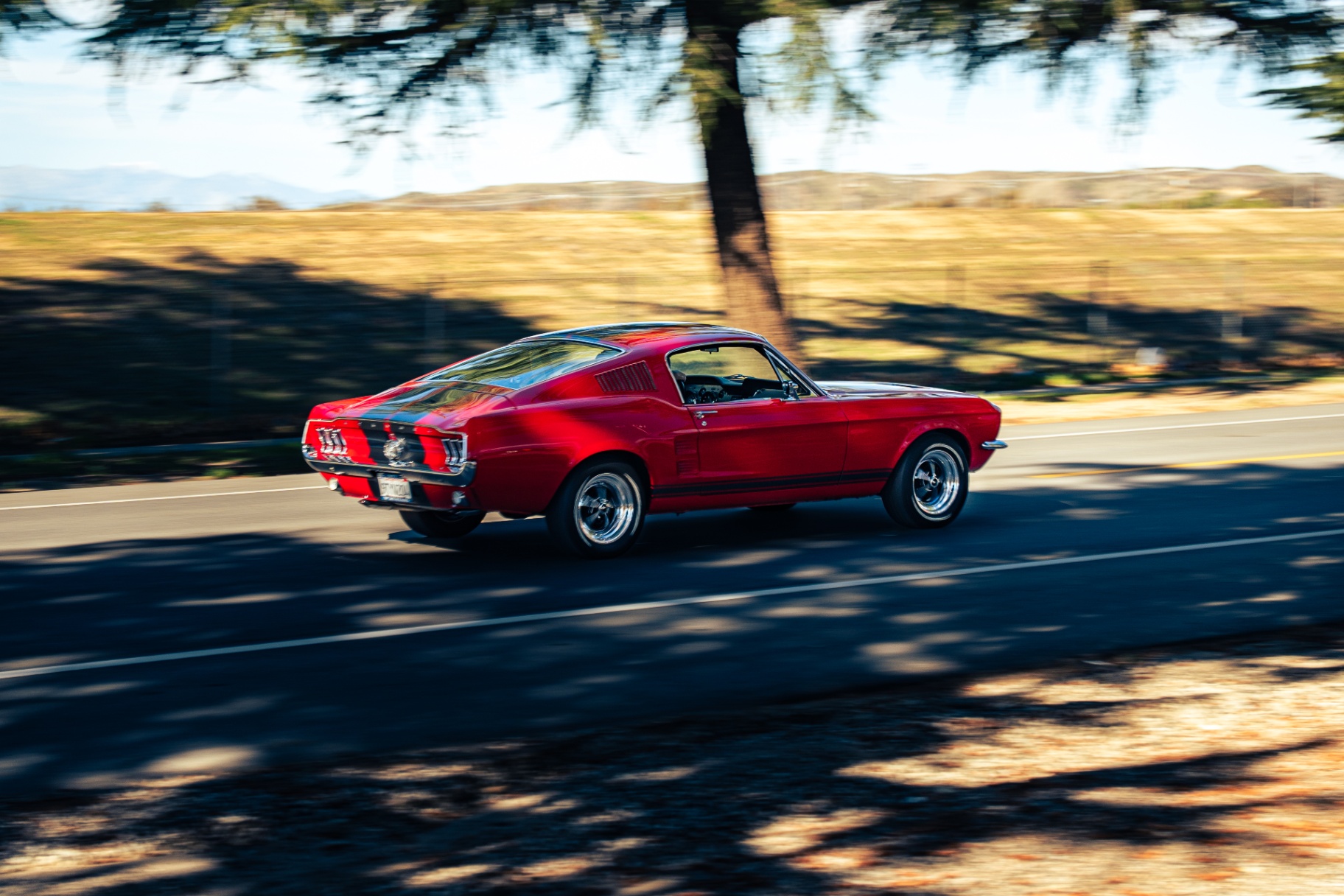 Red 1967 Ford Mustang fastback with racing stripes panning down the road