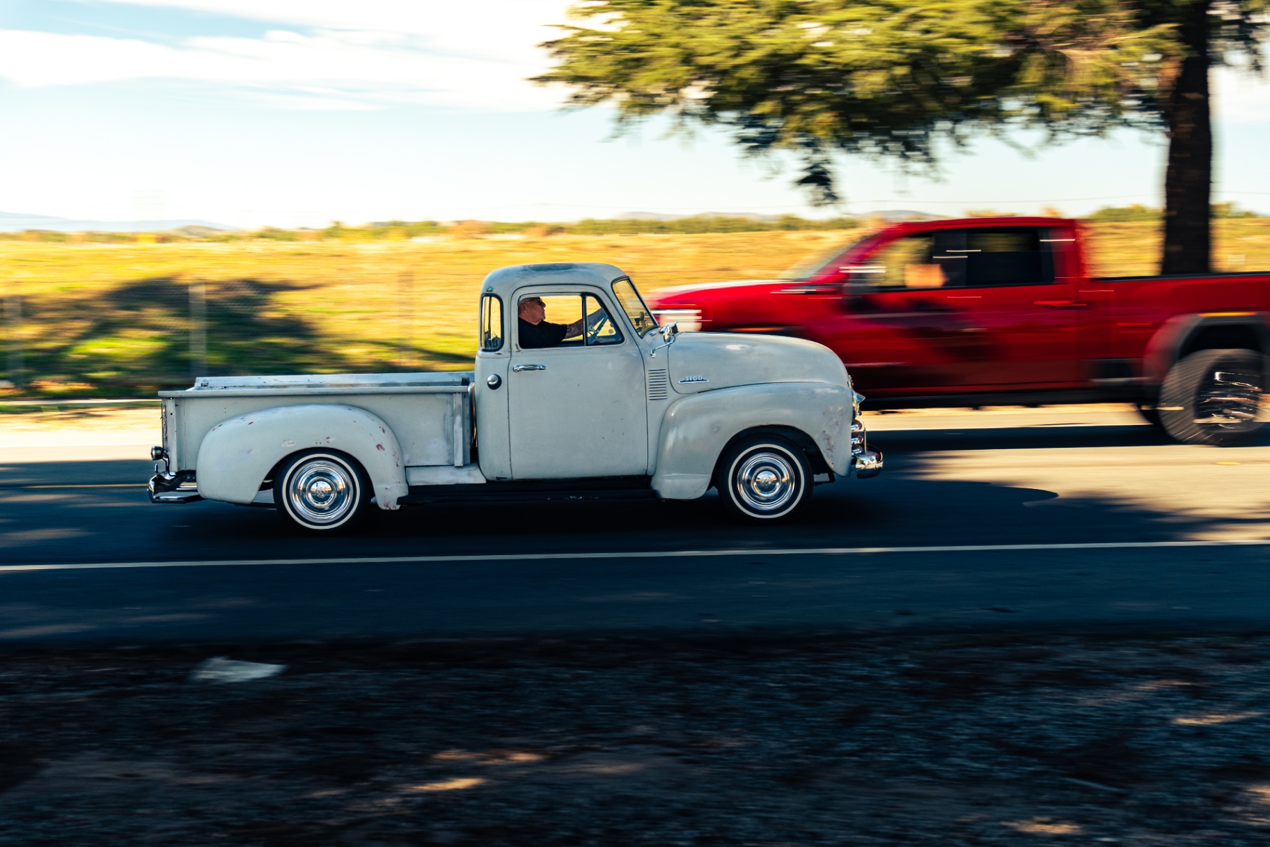 White vintage Chevy 3100 pickup panning past a red modern truck
