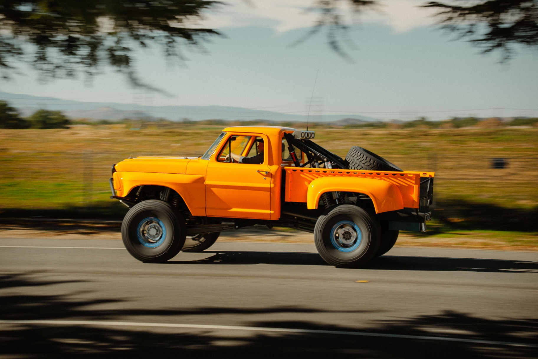 Orange lifted vintage Ford pickup with off-road suspension panning down the road