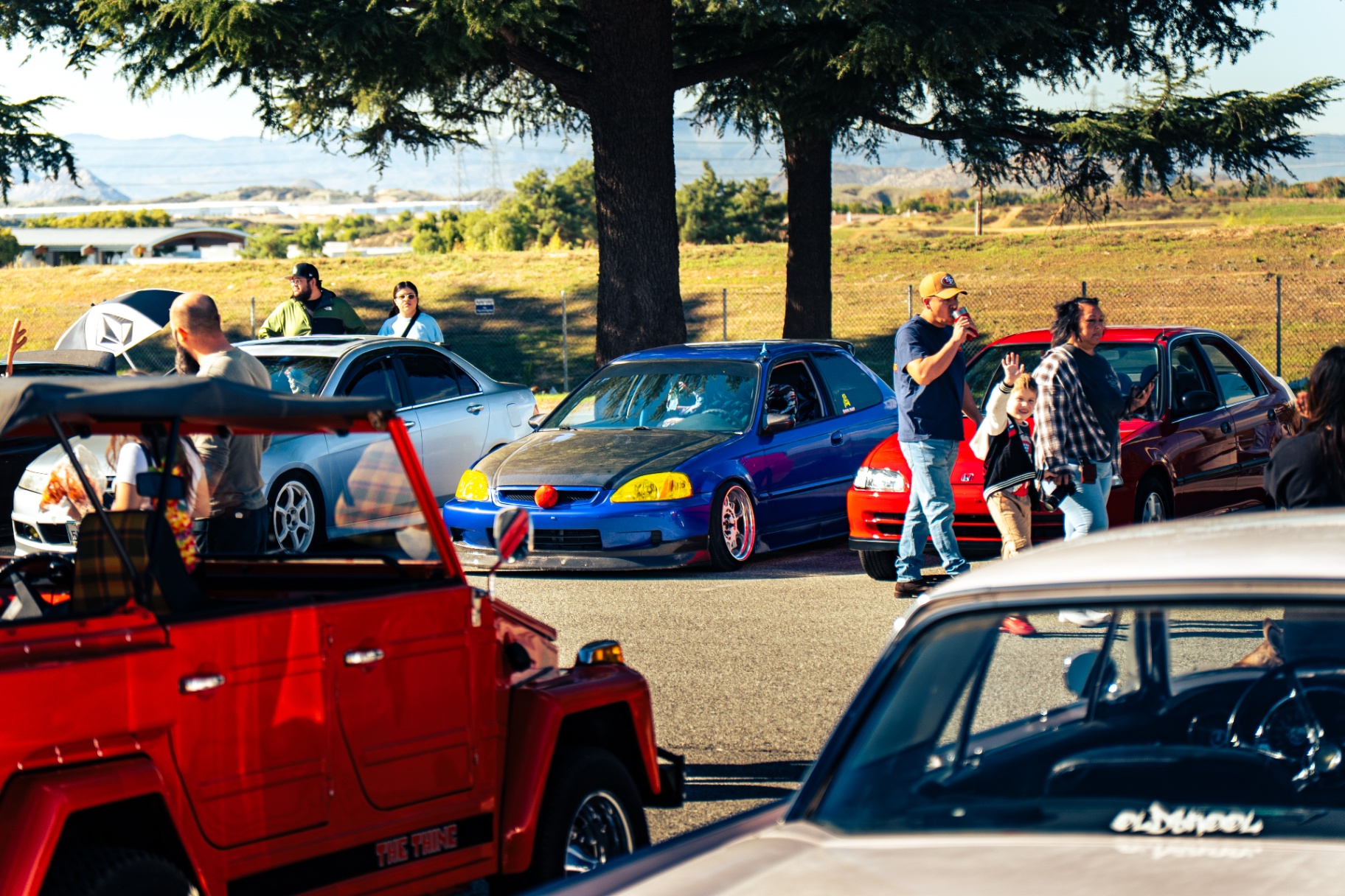Crowd and colorful stanced cars packed into the meet with mountain views