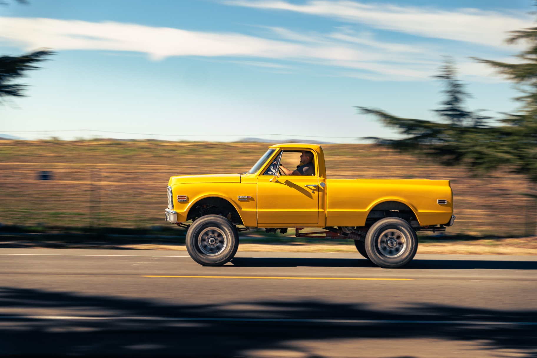 Yellow lifted vintage Chevy C10 pickup panning down the road