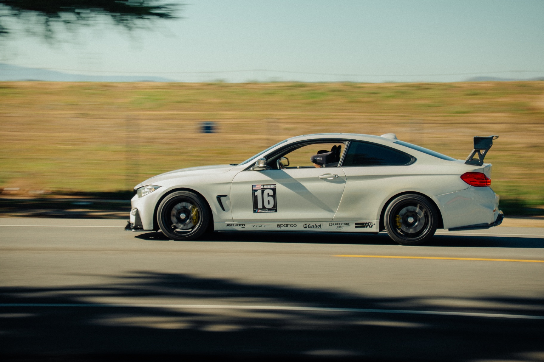 White BMW M4 track car with rear wing panning past golden hills