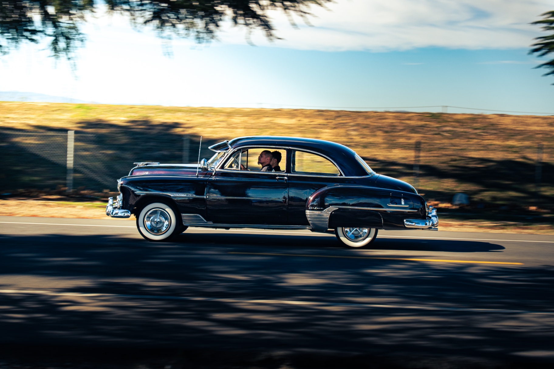 Black 1950s Chevy Deluxe with whitewalls panning down the road