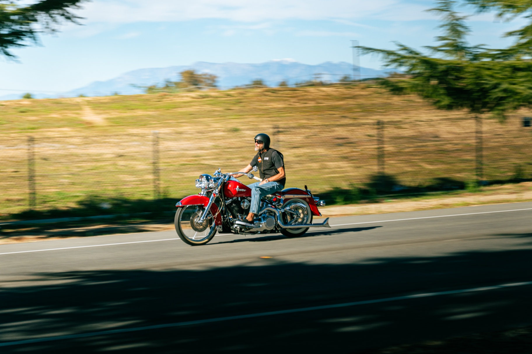 Red Harley-Davidson Softail Deluxe rider cruising with mountain backdrop