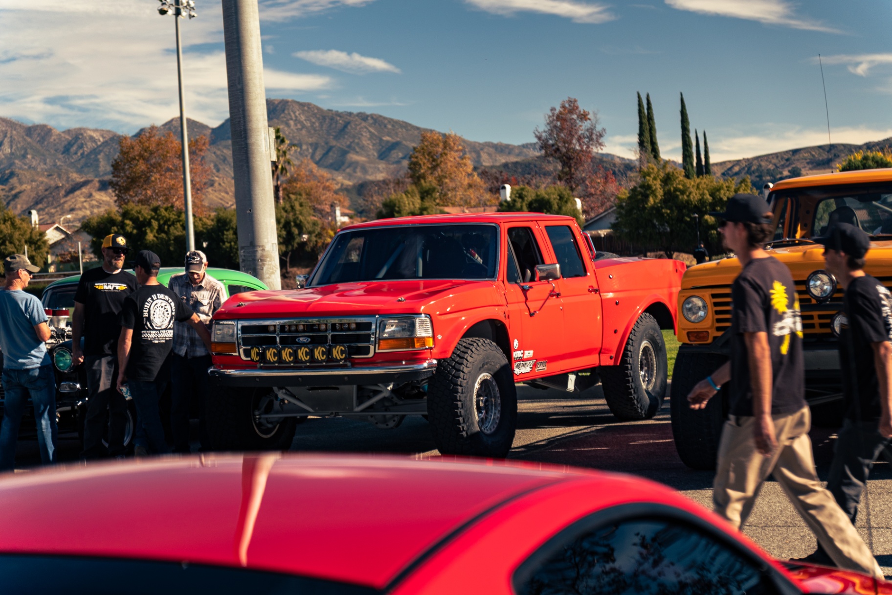 Red prerunner Ford truck between a green muscle car and yellow Bronco with the mountains behind