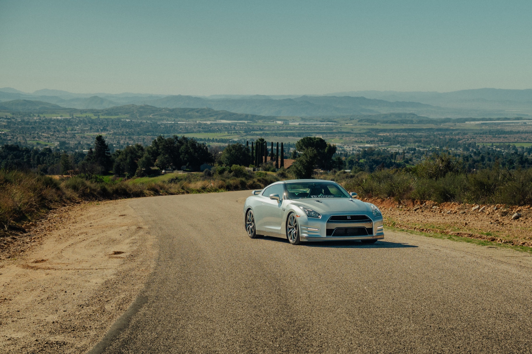 Silver Nissan GT-R on a hilltop road overlooking the valley