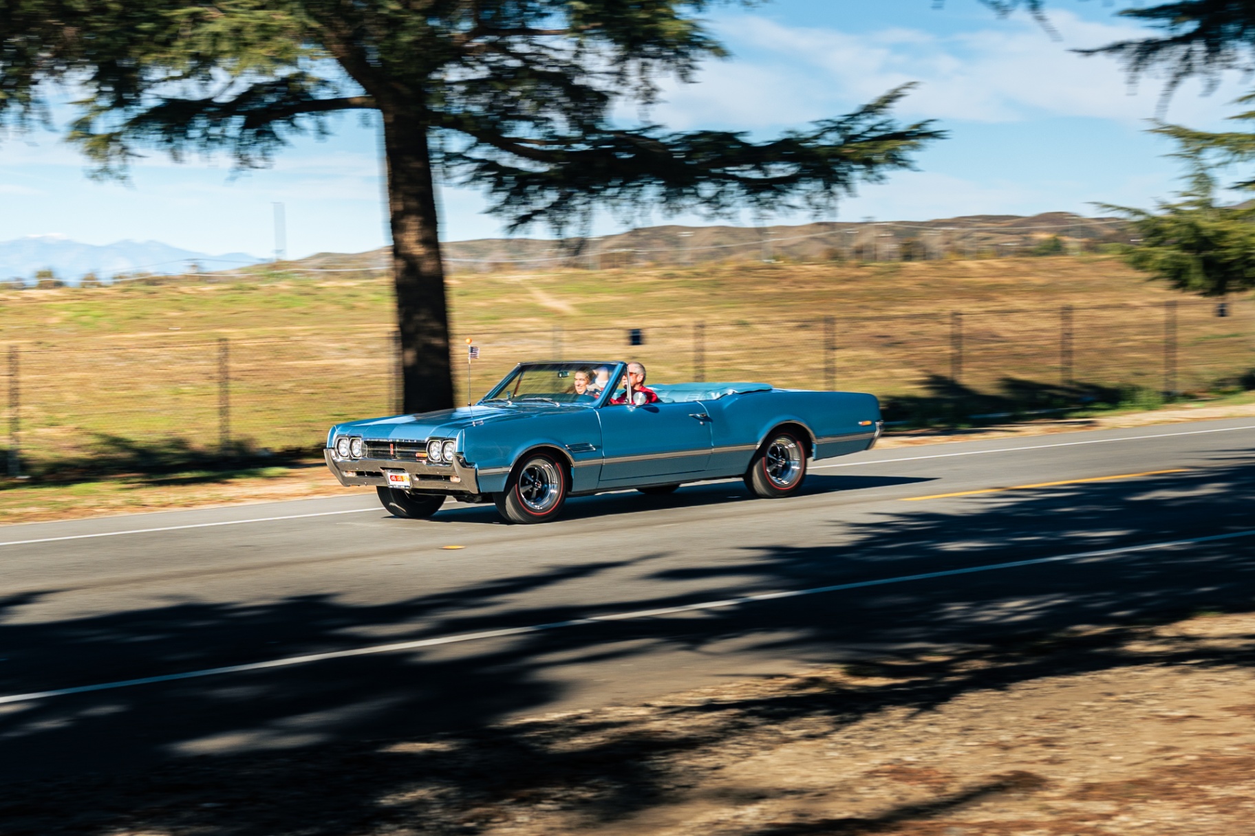 Blue Oldsmobile 442 convertible with an American flag cruising past the hills