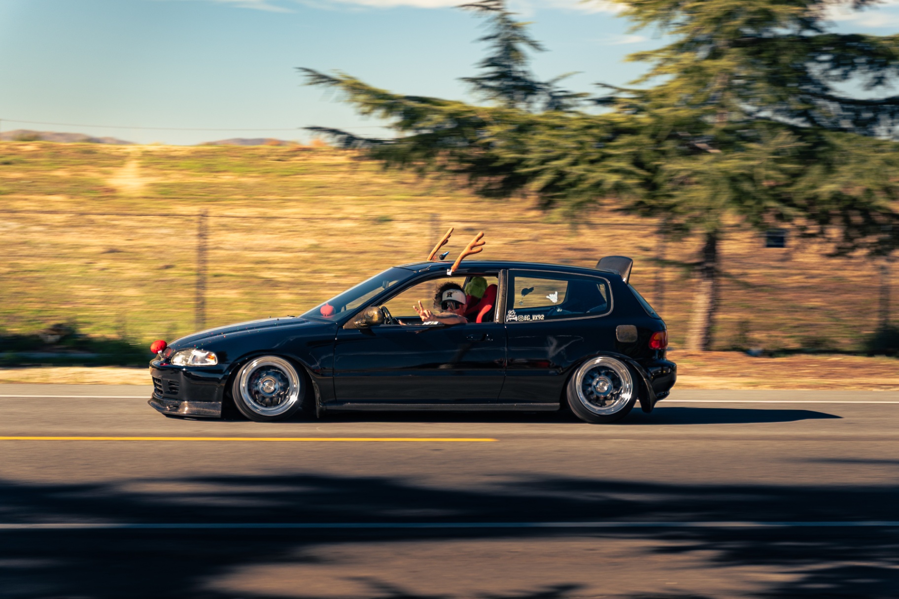 Slammed black Honda Civic EG hatchback with reindeer antlers cruising down the road