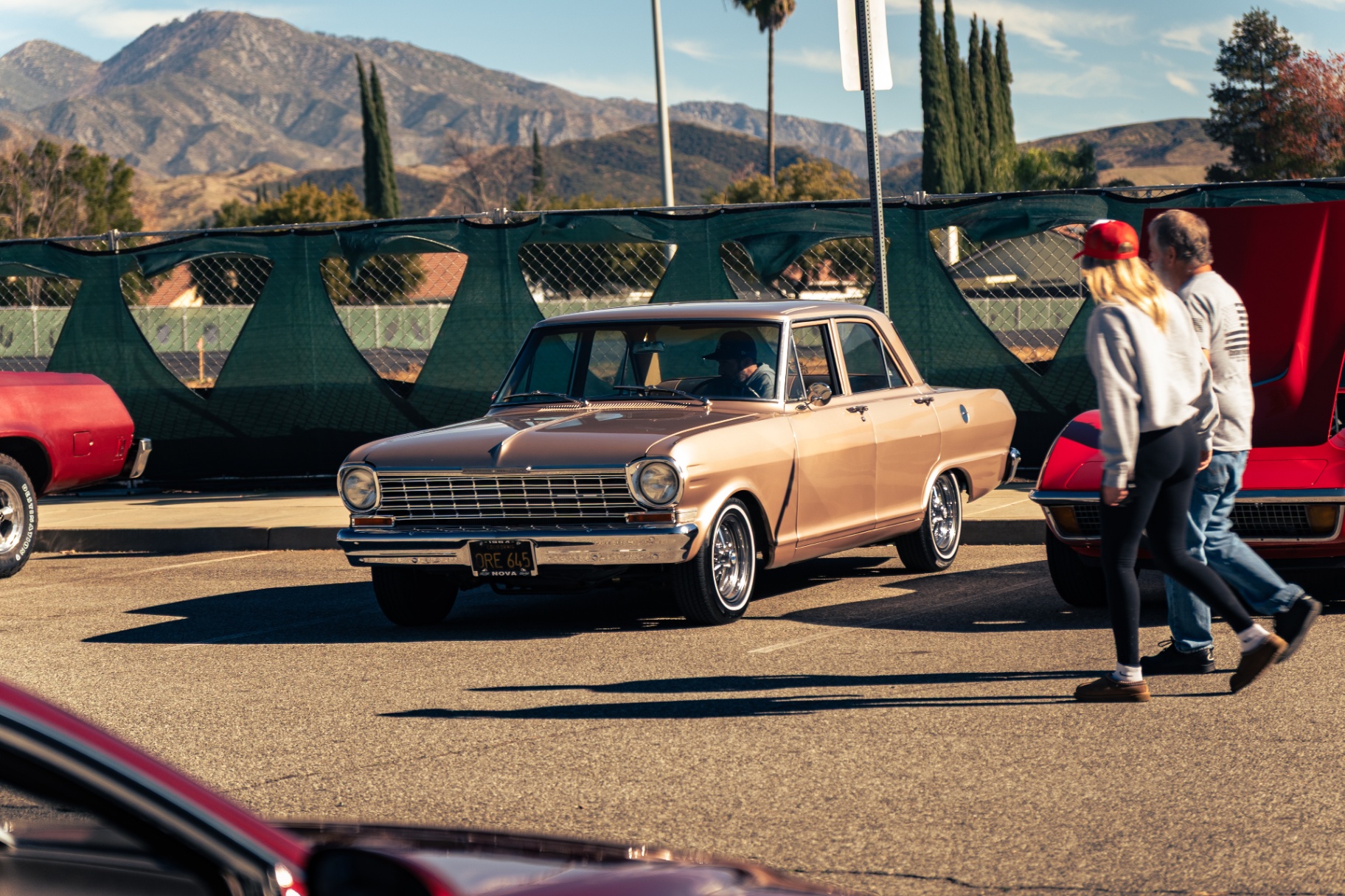 Champagne classic Chevy Nova sedan rolling into the meet with mountain backdrop