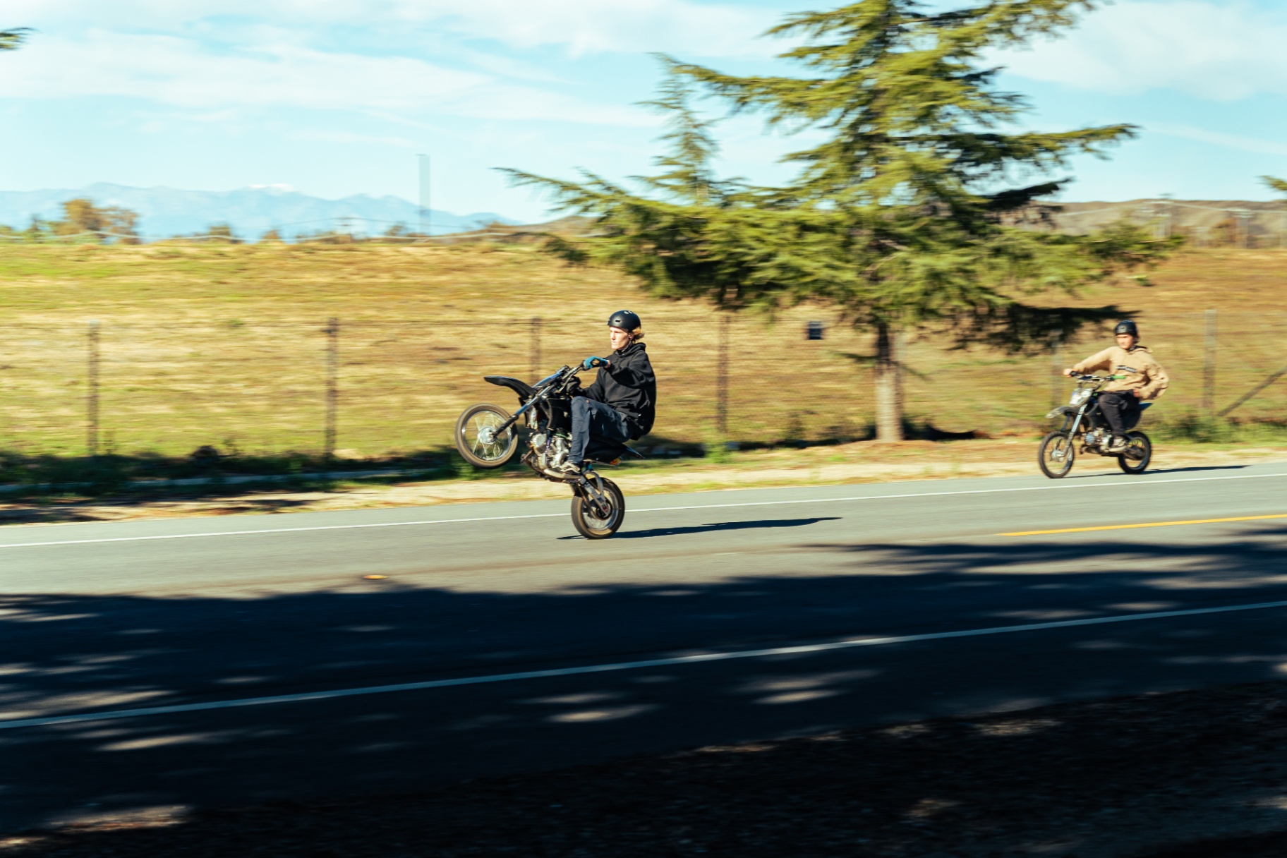 Pit bike rider pulling a wheelie down the road next to a second rider