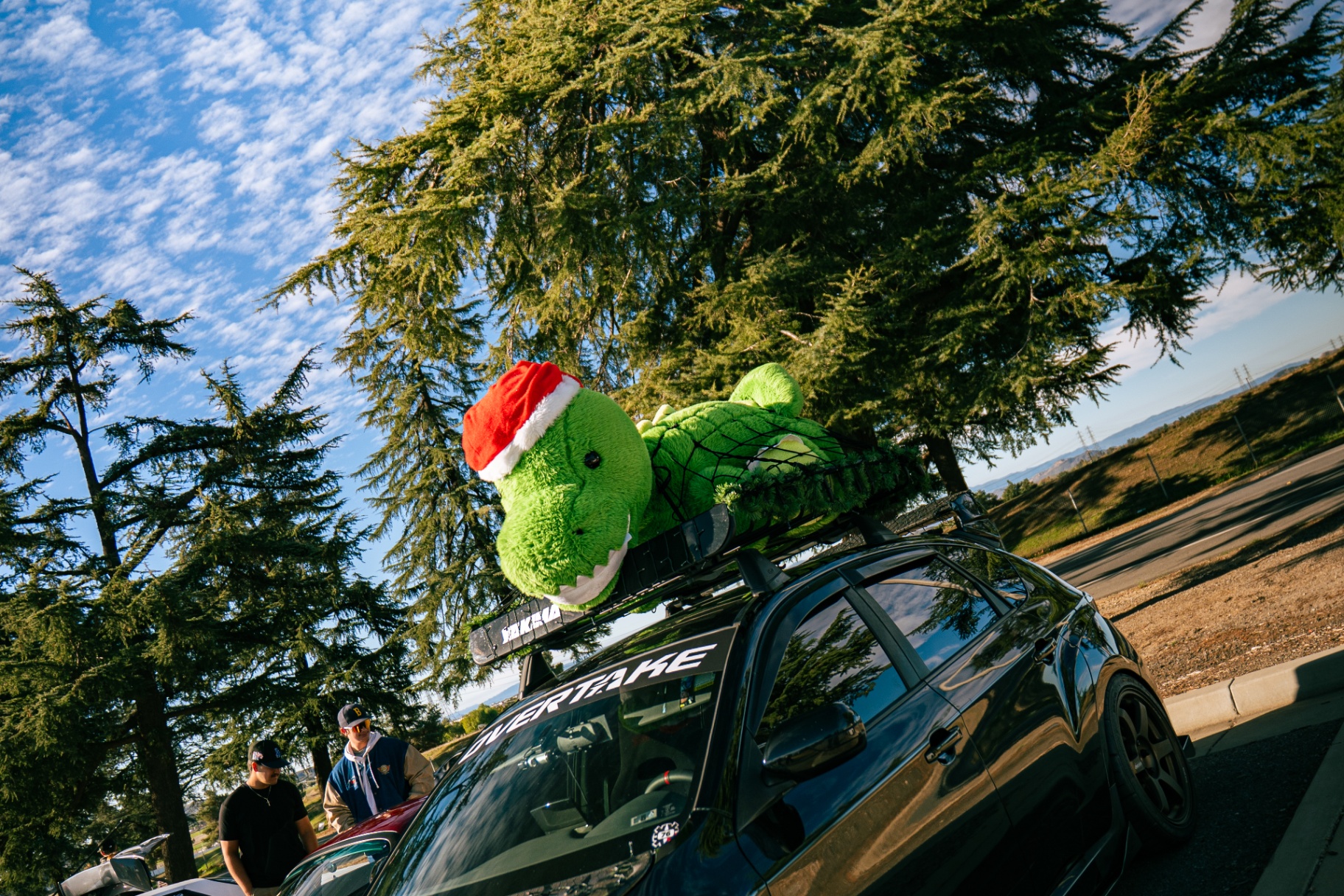 Plush dinosaur riding on a lowered black hatchback at sunrise