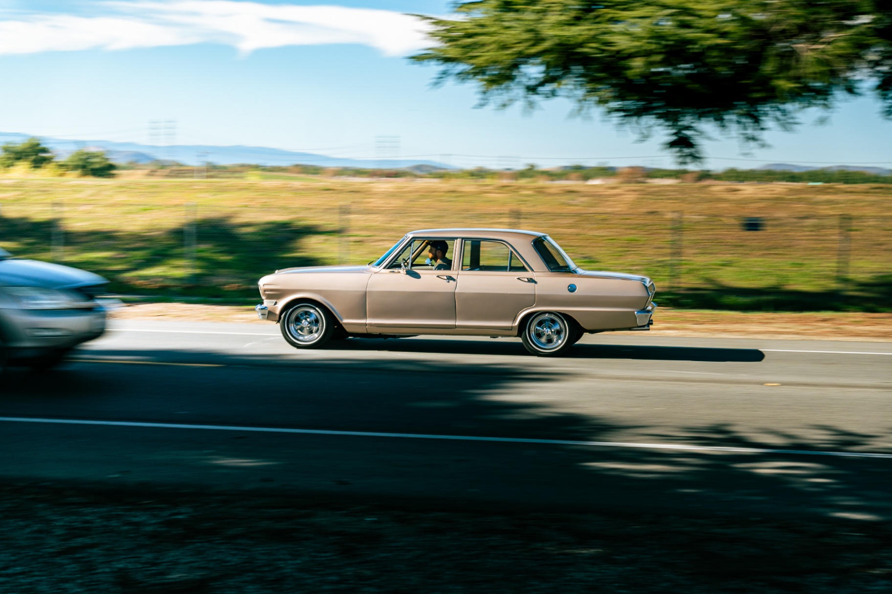 Rose gold classic Chevy Nova sedan panning down the road