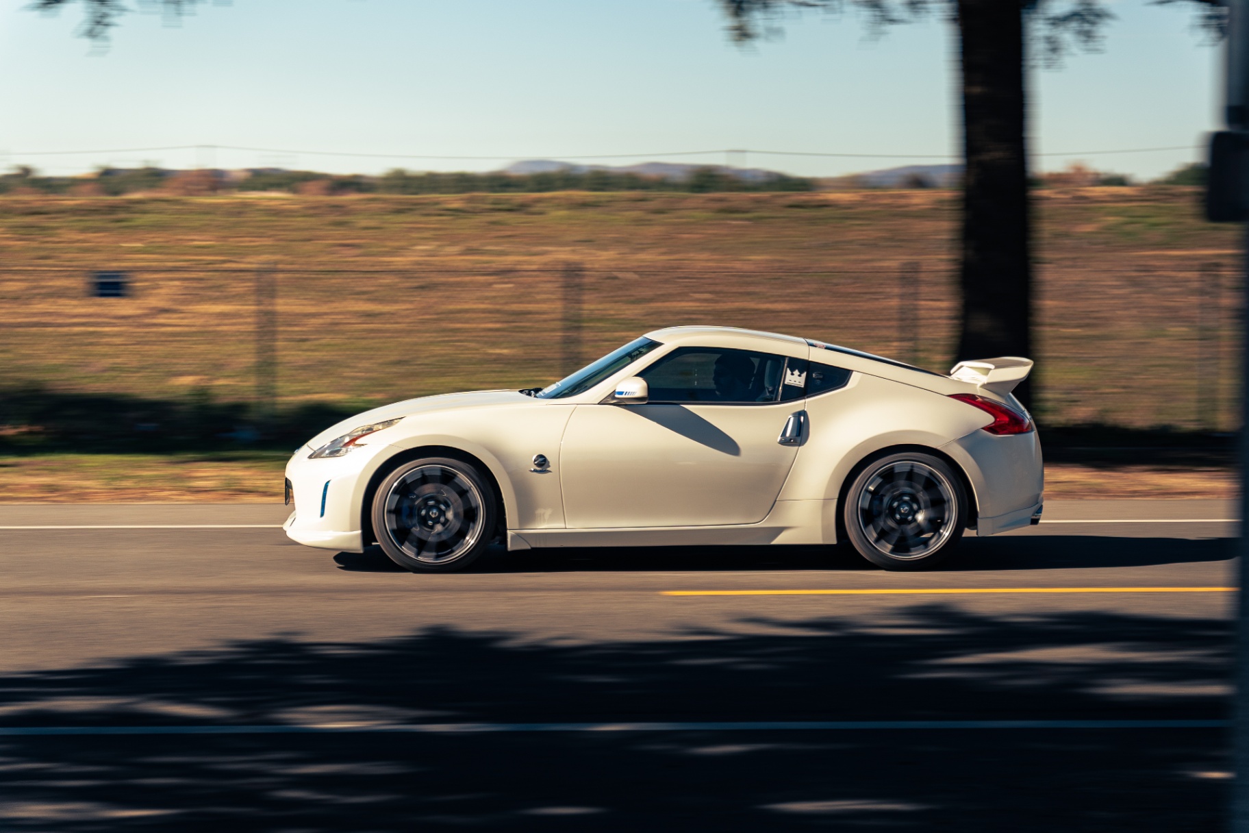 Pearl white Nissan 370Z panning past golden hillsides at sunset